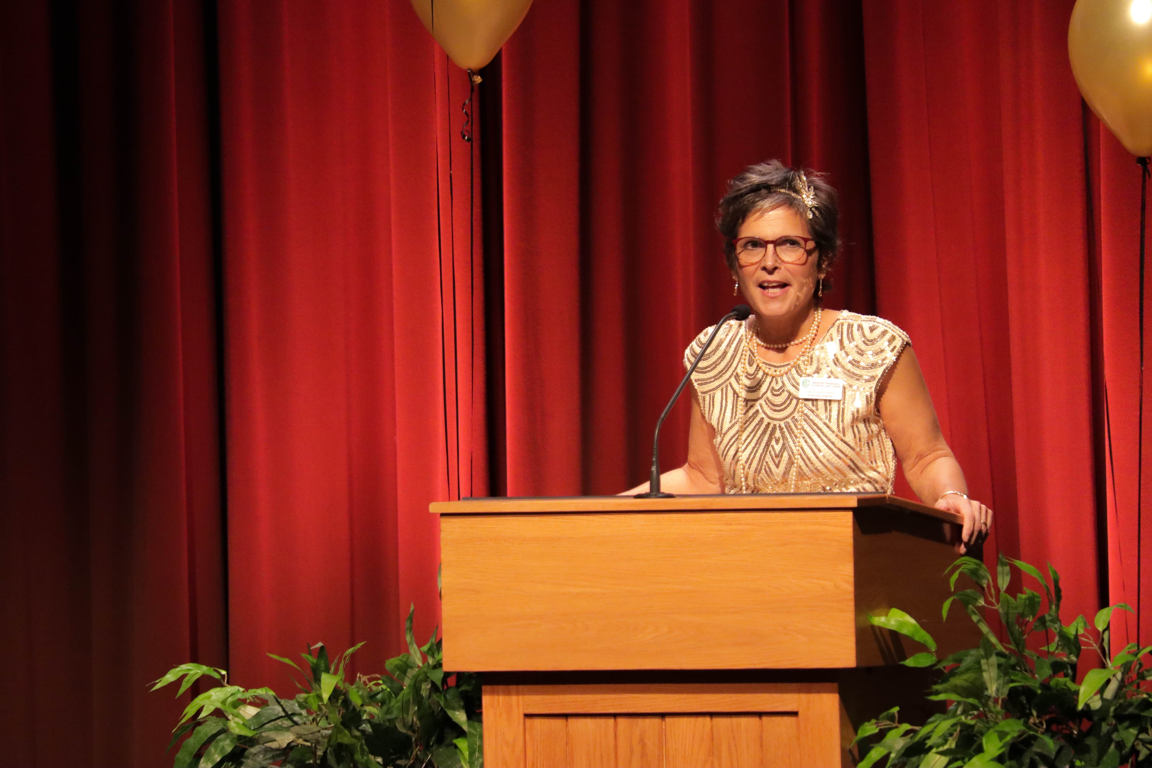 A woman speaking at the podium in front of a red curtain