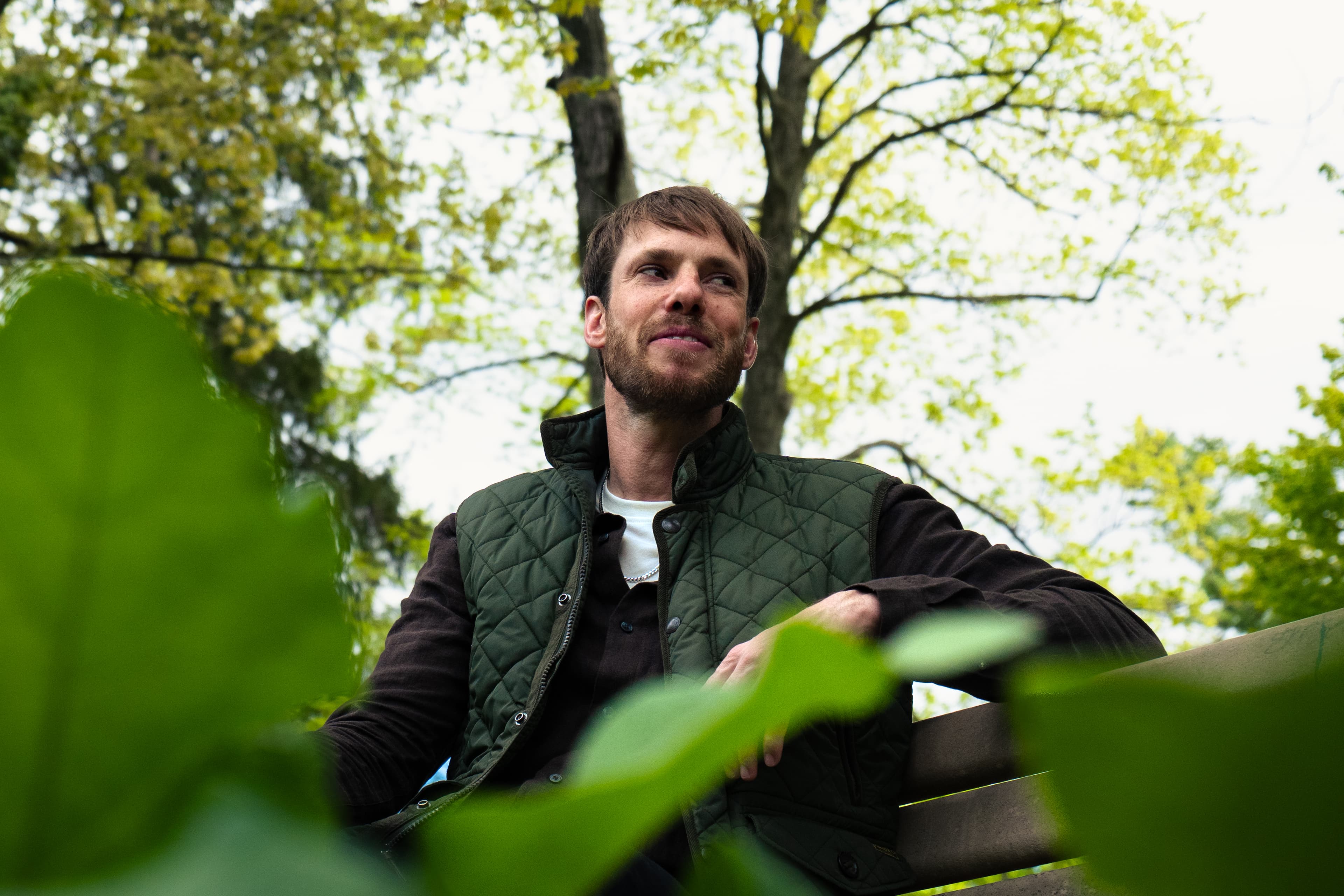 Low-angle photo of a man on a park bench, leaves in the foreground