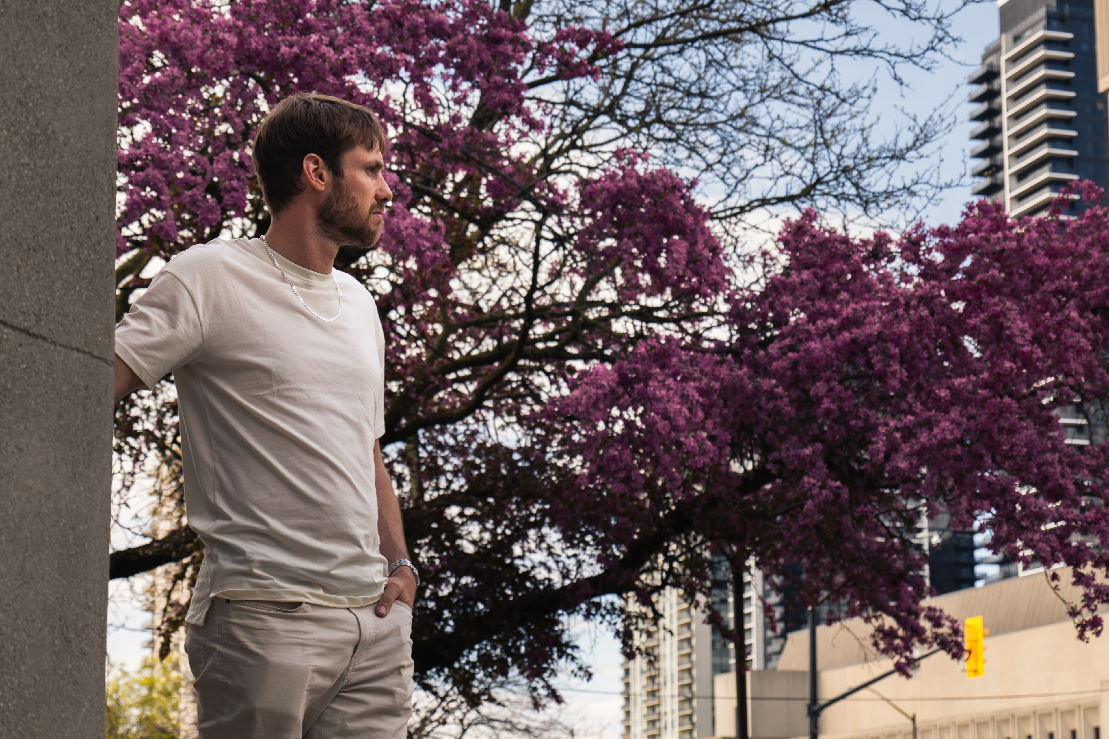 Man standing beside a purple blossoming tree with a city skyline behind